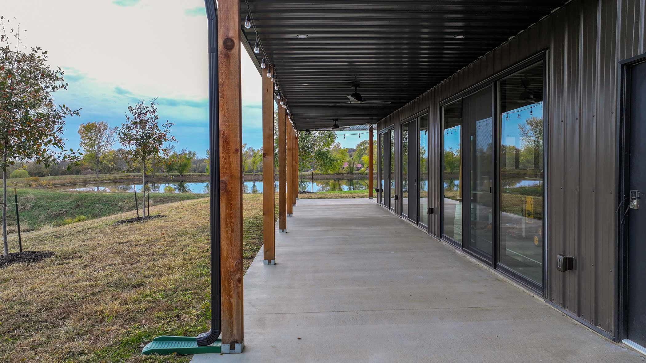 Full-length covered porch at Red Bird Ranch — cedar posts, string lights, concrete floor, sliding glass doors, and open field views