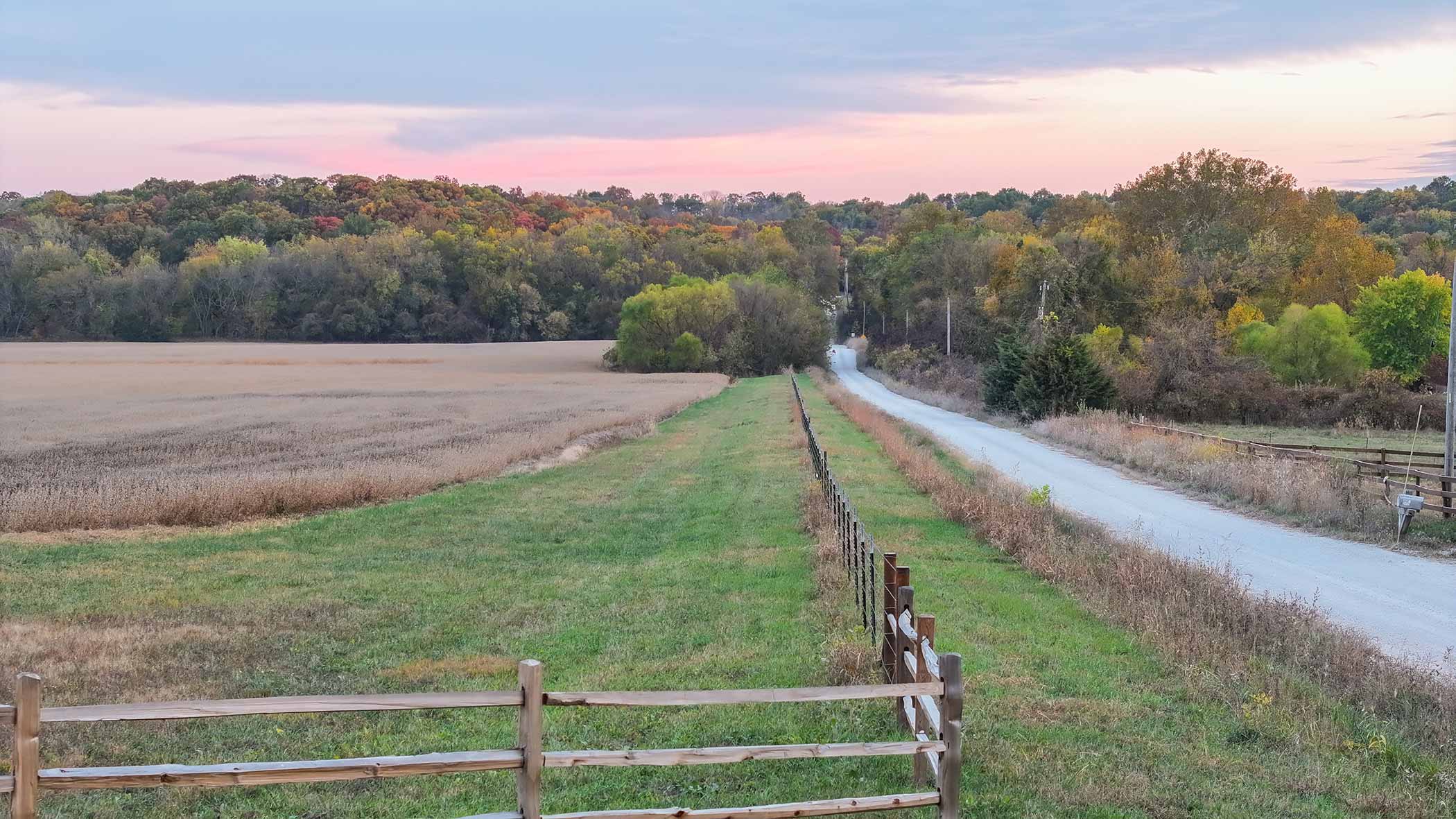 Entry road at dusk — split-rail fence, pink Kansas sky