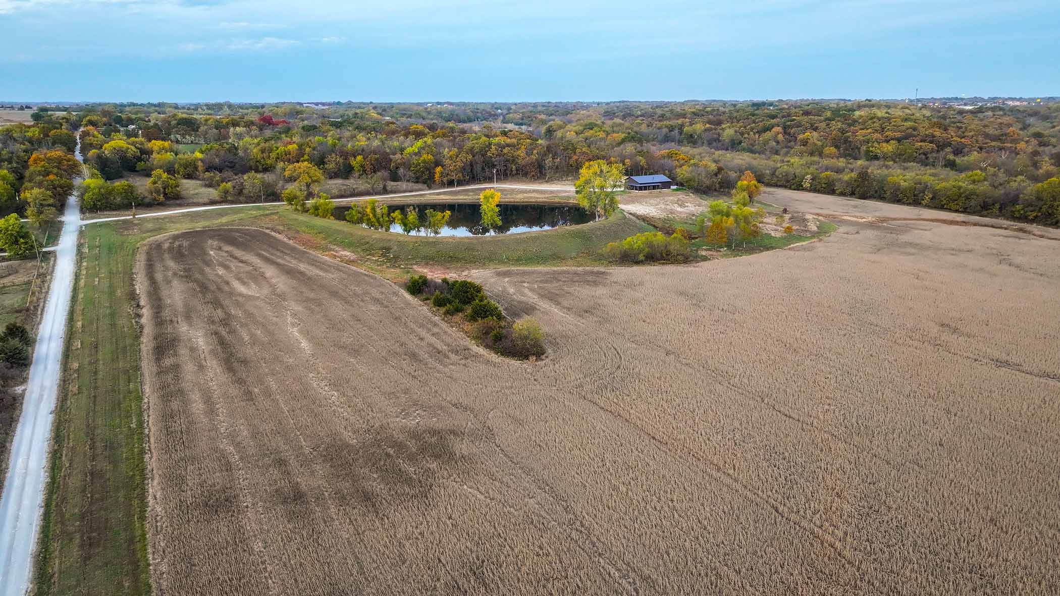 Aerial view of Red Bird Ranch — large harvested field, pond center-left, the building visible in the upper right, entry road at far left