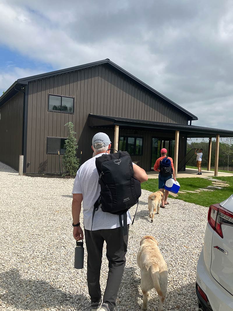 Corporate guests arriving at Red Bird Ranch with dogs — dark modern building, gravel drive, premium first impression