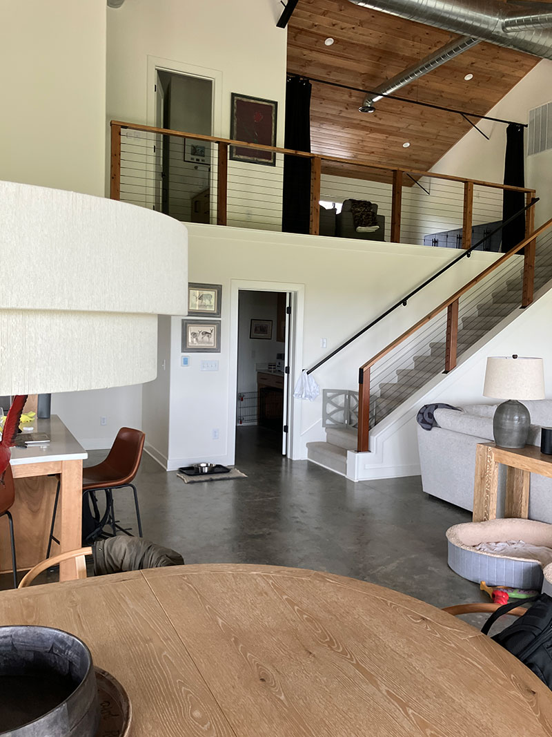 Great room overview — cable railing mezzanine loft, round dining table, leather bar stools, vaulted ceiling