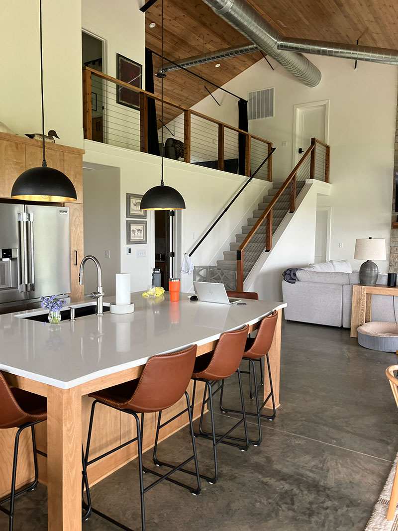 Kitchen island with black dome pendant lights, leather bar stools, and quartz countertop — great room and mezzanine behind